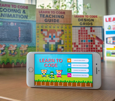 Learn to Code game app on an iPhone with Learn to Code books in the background.